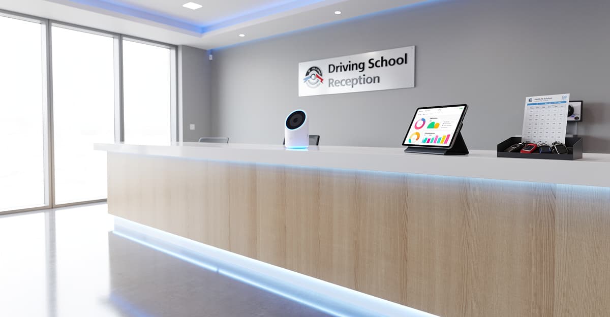 Assistant vocal auto-école posé sur un bureau d'accueil moderne avec tableau de bord IA et clés de voiture